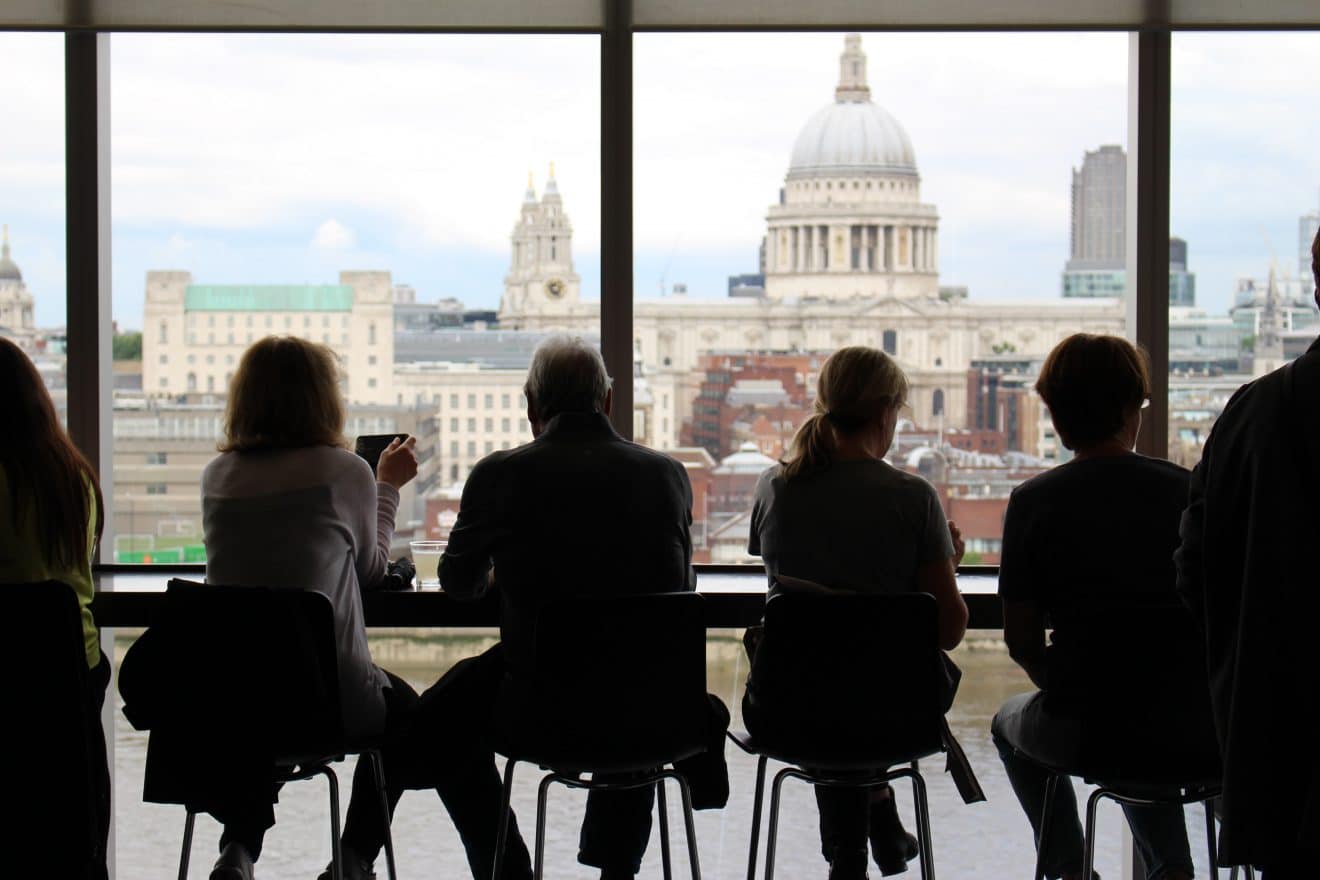 A group of people, sitting in an office with an amazing view of St. Paul's Cathedral in London, networking whilst drinking tea.