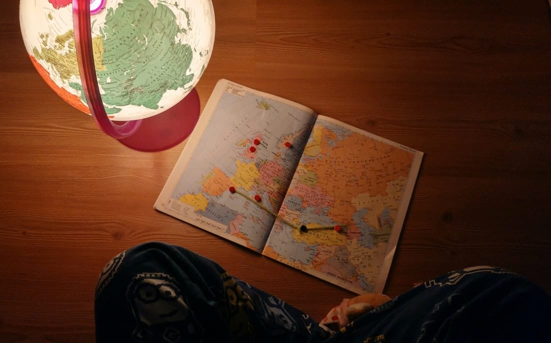 Image of globe lightbulb and paper atlas on a desk.