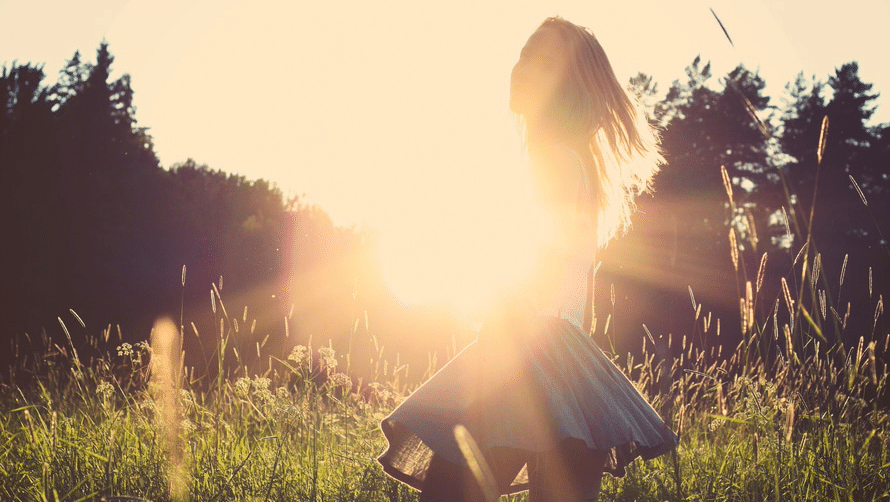 Image of a woman in a field with the suns rays shining past her.