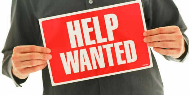 Image of a man holding a red sign that writes 'HELP WANTED' in Capital letters.