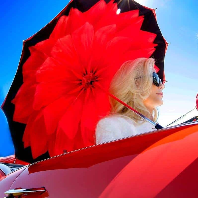 Carolyn Mullany Jackson holding a red umbrella to block the sun near a red car.