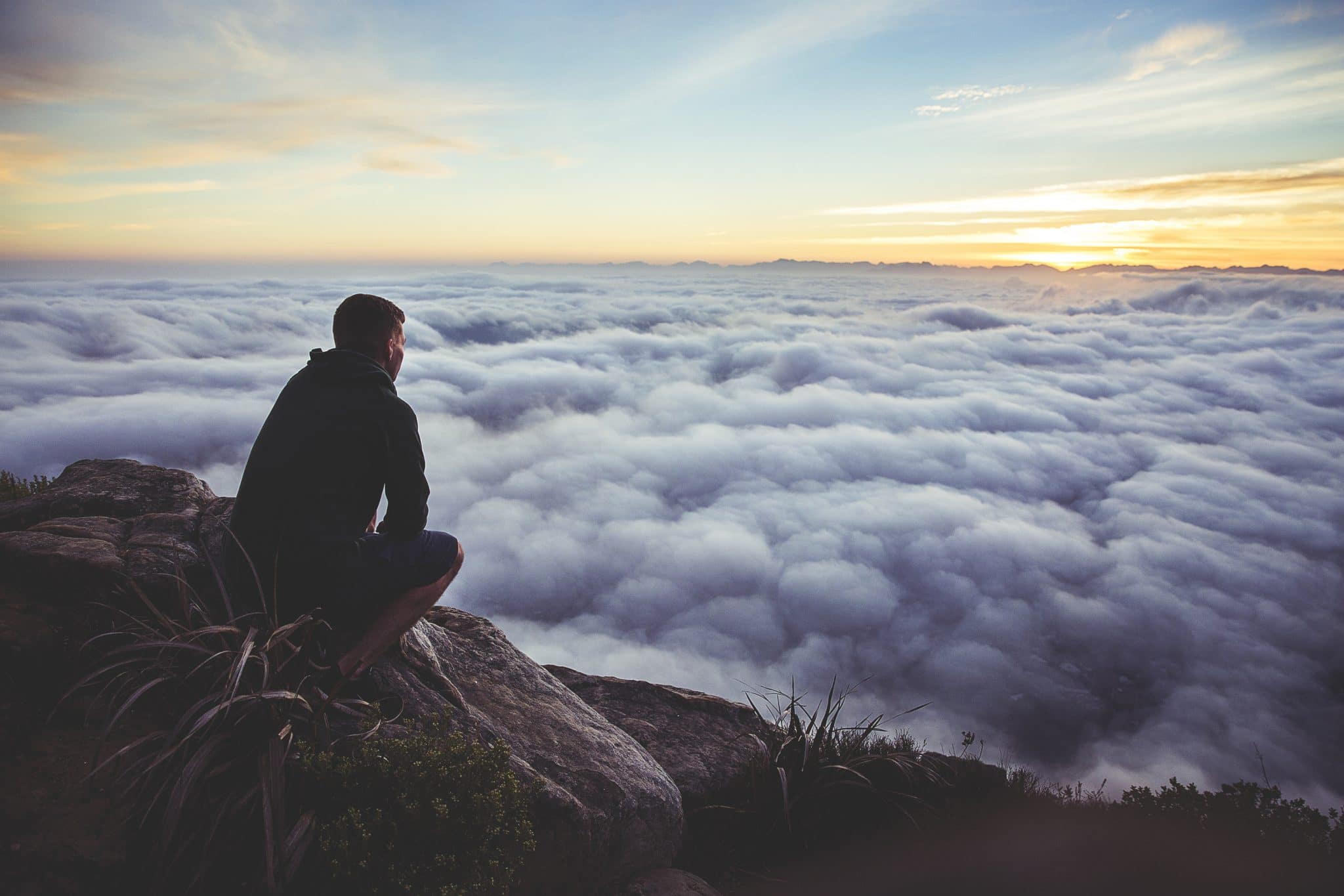 Man sitting on top of the mountains looking into the many clouds below him