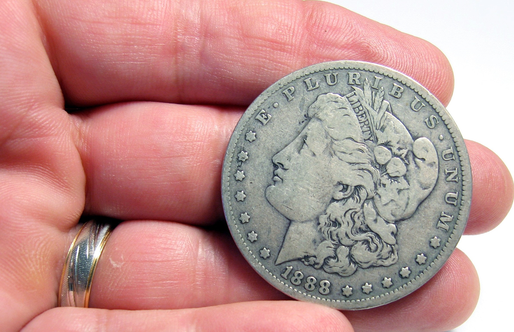 Photo of a man holding an old silver liberty dollar on his fingertips.