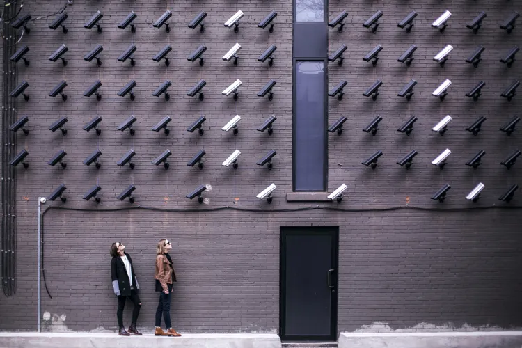 Dozens of cameras on a wall surveilling people who walk past.