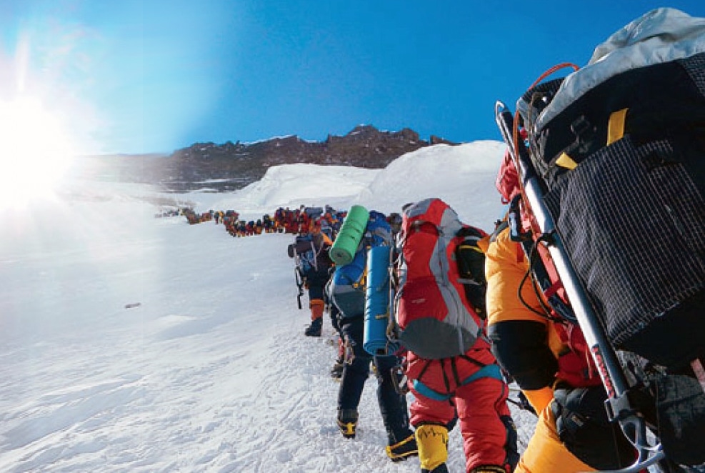 Photo of a big group of people with lots of backpacks and kits climbing icy Mount Everest.