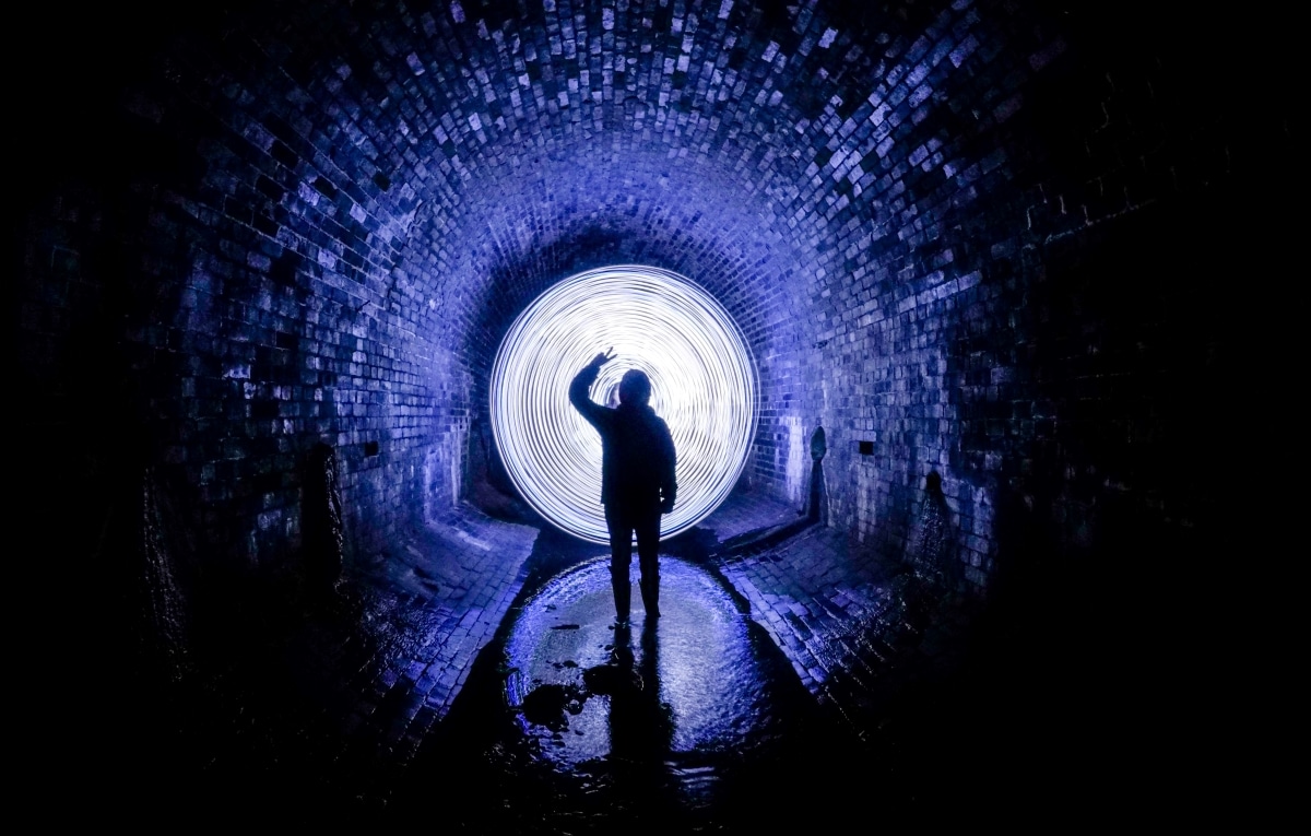 Photo of person walking through a tunnel with an amazing blue light in the background