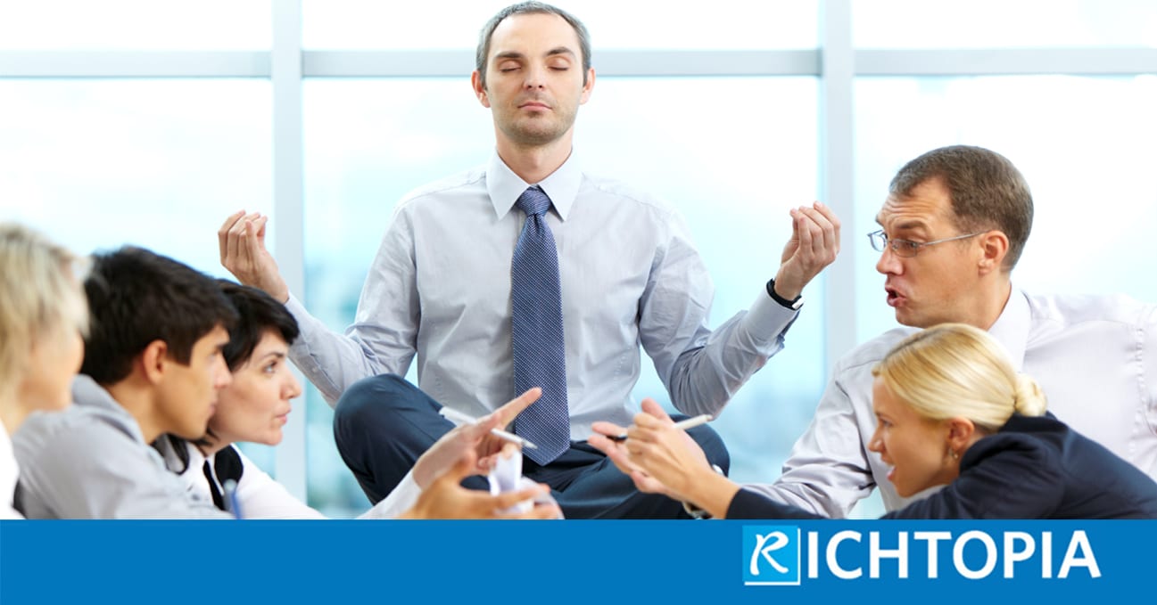 Article about toxic behaviour in the workplace. Picture of man in business suit sitting on a table in the middle of a meeting meditating with his legs crossed and hands praying posture, whilst 5 of his colleagues argue on the same table around him.