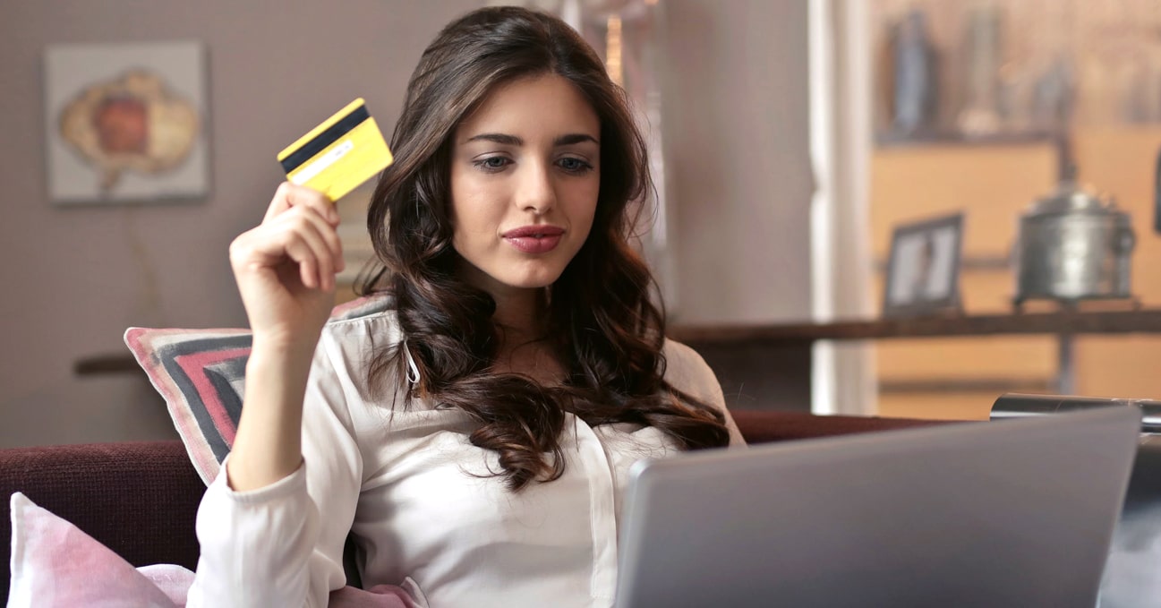 Photo of an Asian woman sitting down a chair, facing her laptop on the table, with her credit card in hand, ready to make an international money transfer.