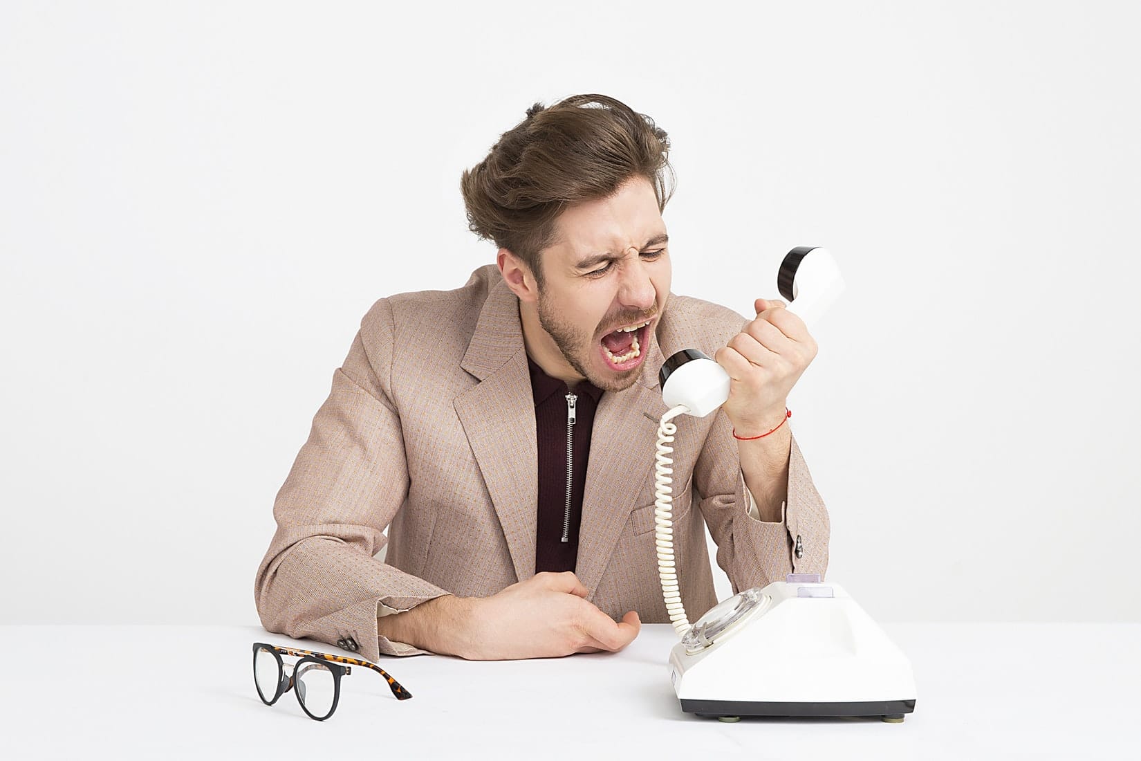 Angry man in a suit, sitting on his desk, screaming into a telephone.