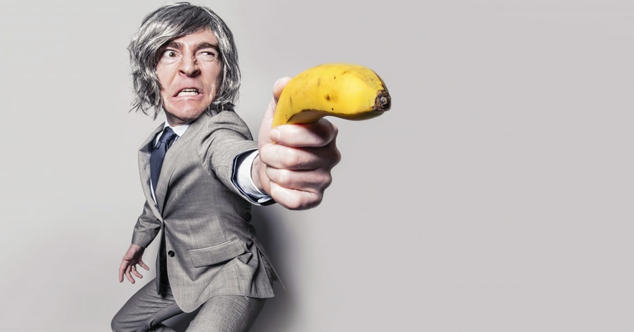 Man in grey suit looks crazy and holding a banana like a gun for Richtopia article about learning from bad leaders