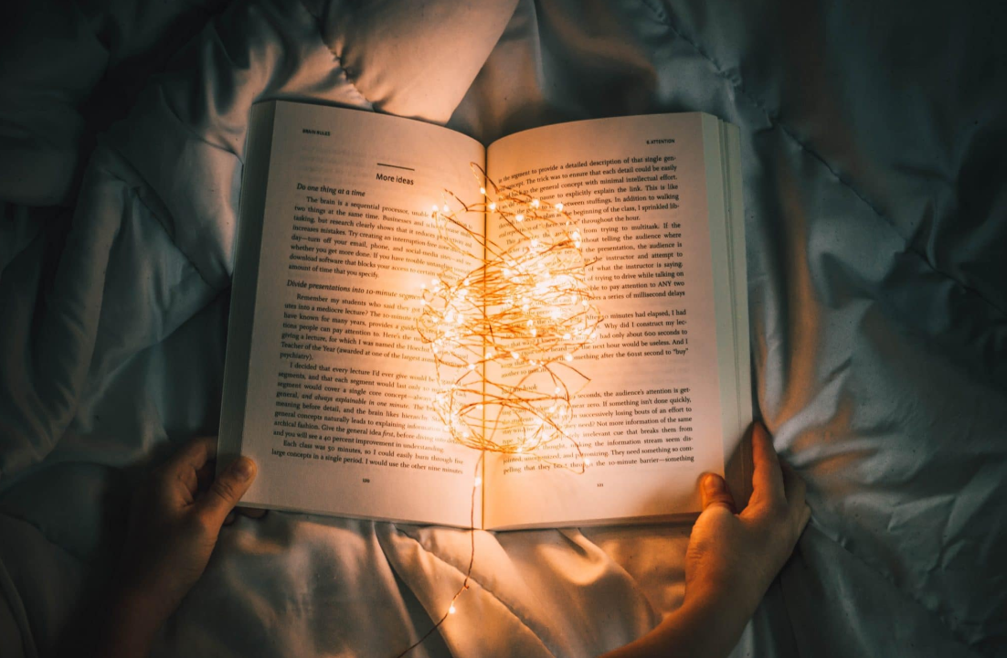 A person reading a book in the dark whilst on their bed with led lights inside the middle of the book