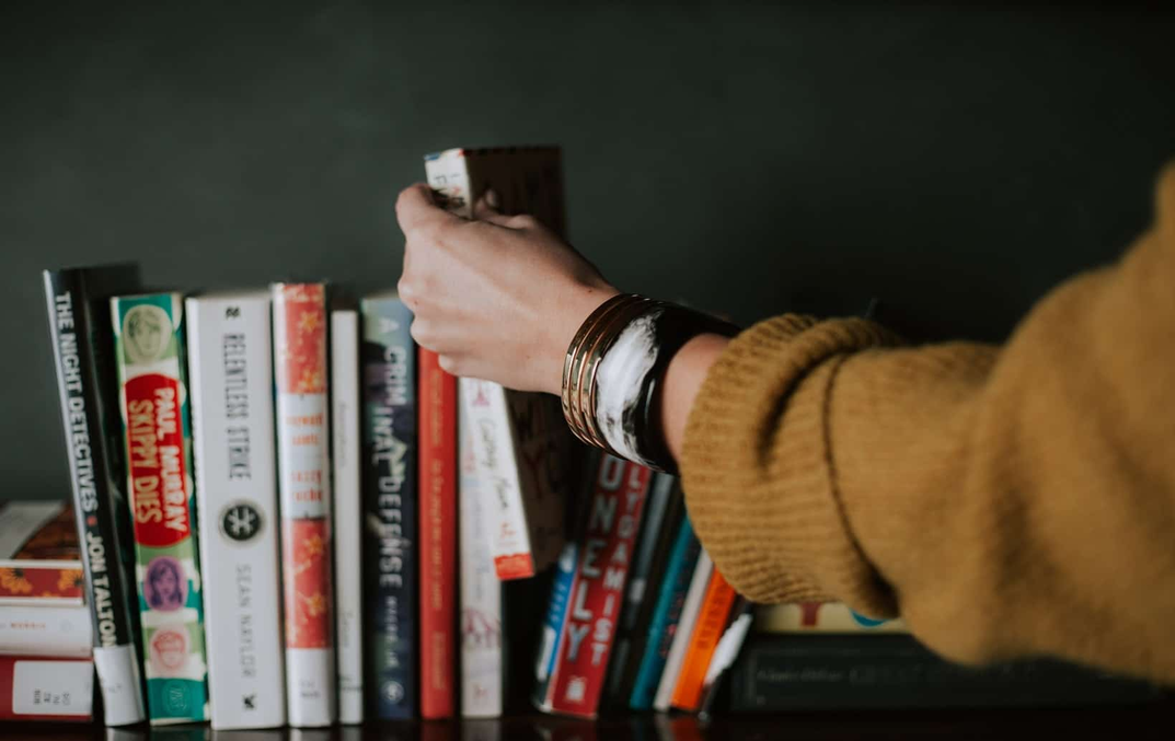 Photo of a woman's hand with cool bracelets, picking a book up from her home-library