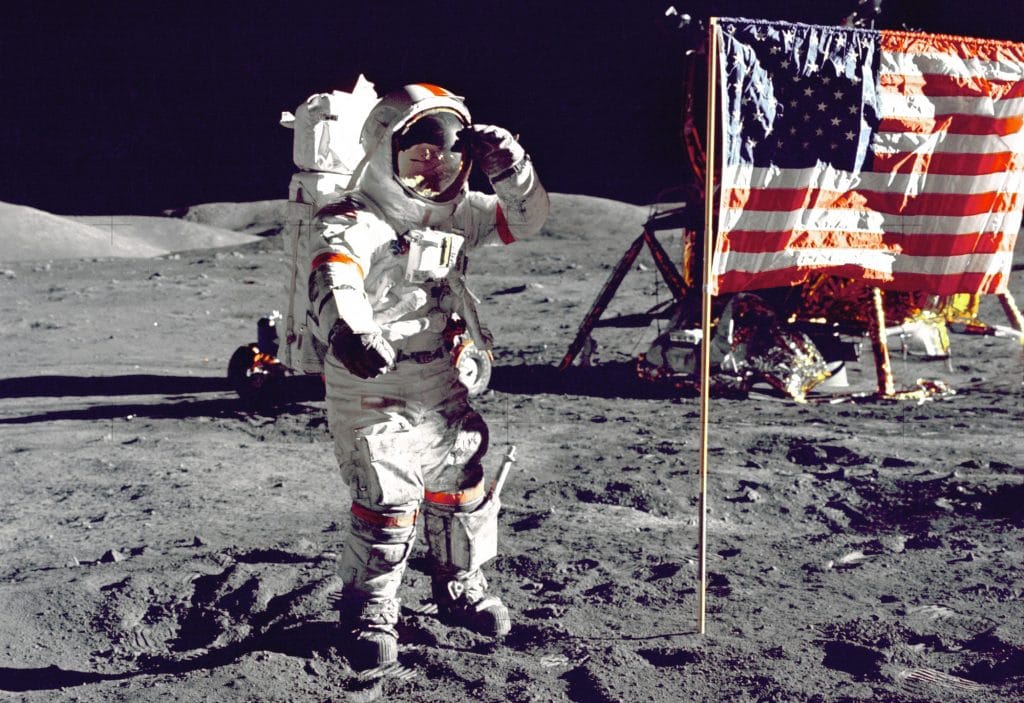 Astranaut on moon's surface, saluting next to American flag.