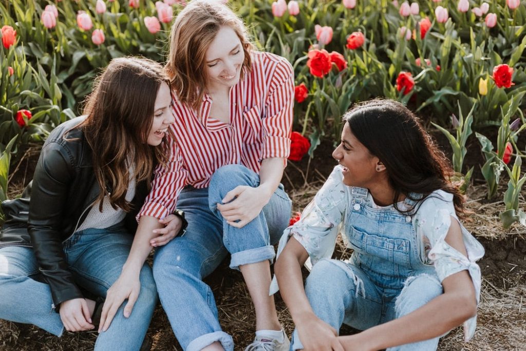 Three women sitting by flowers, all smiling and having a humble conversation.