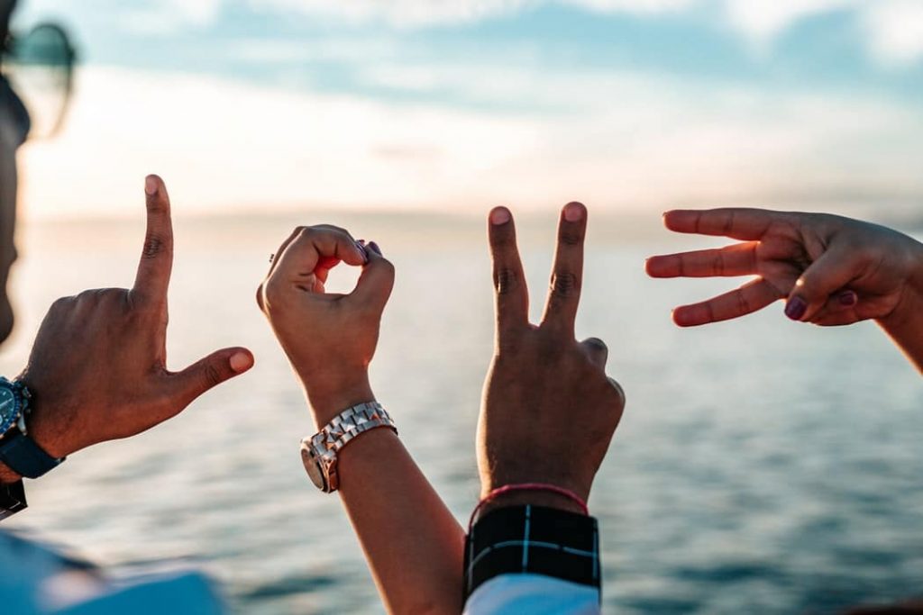 Photo of 4 people on the beach, each holding out their hands to spell "LOVE".