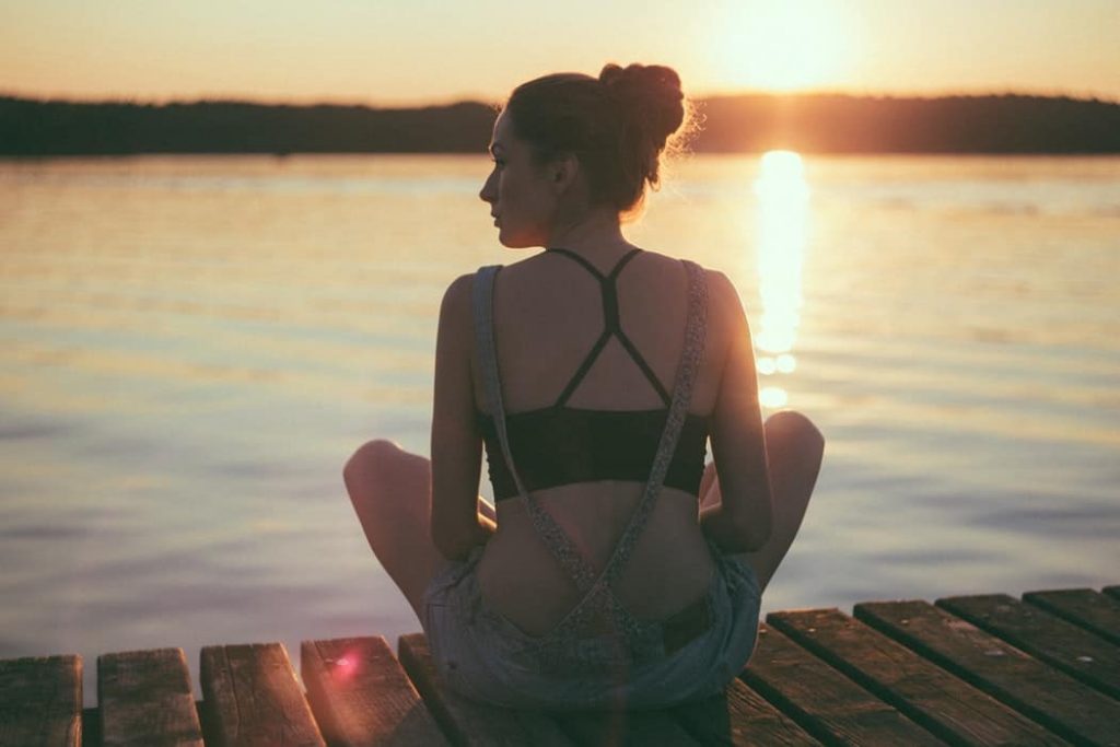 Woman sitting on the dock at sunset, thinking deep.