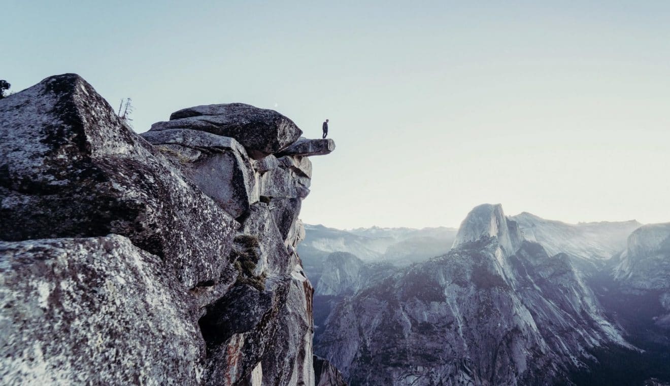 Man standing on a cliff edge to look at the awe inspiring view of ice-covered mountains.