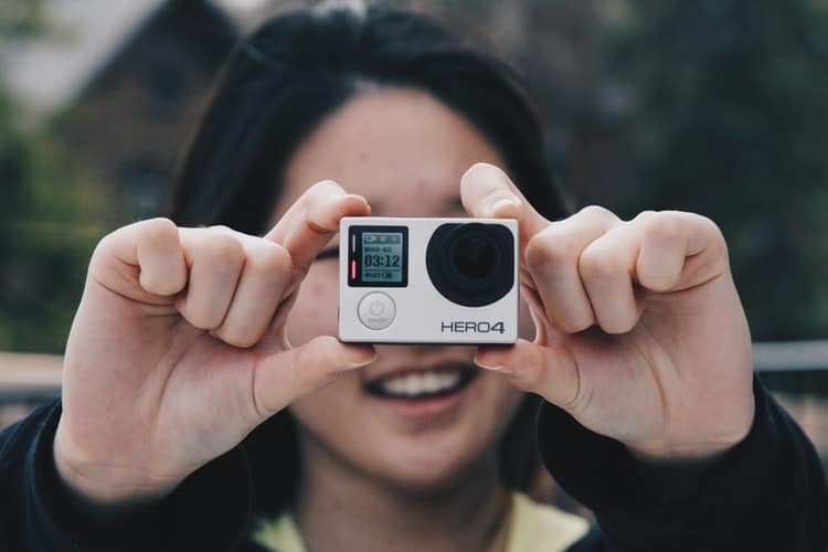 Woman smiling whilst snapping a photo on her GoPro 'Hero4' camera.