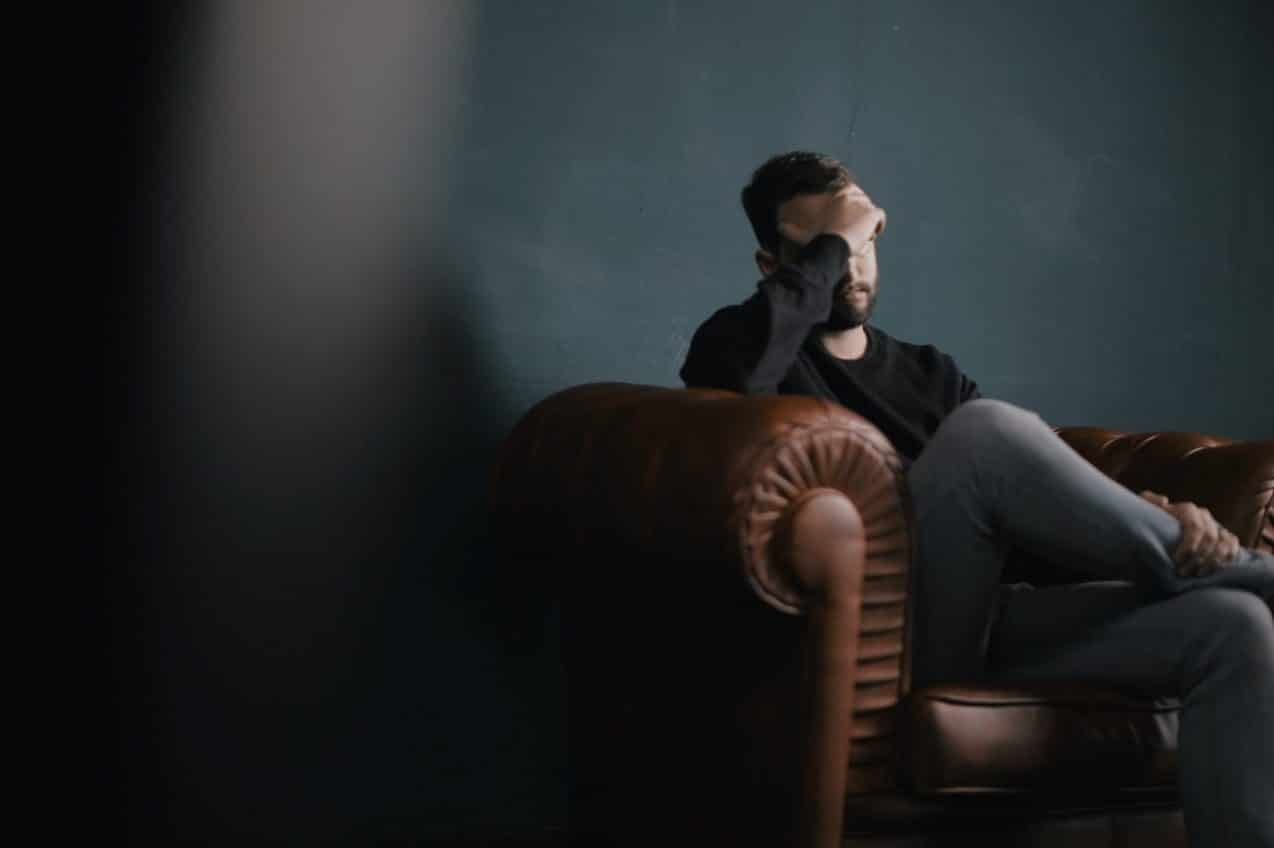 Man sitting on a leather sofa, holding his head in confusion