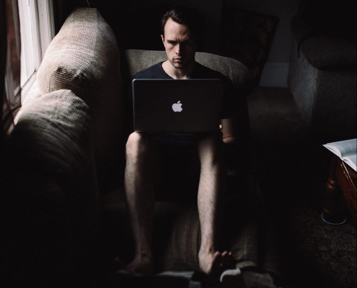 Man sitting alone on his living-room sofa, using his Macbook Pro to socialise instead of doing it physically