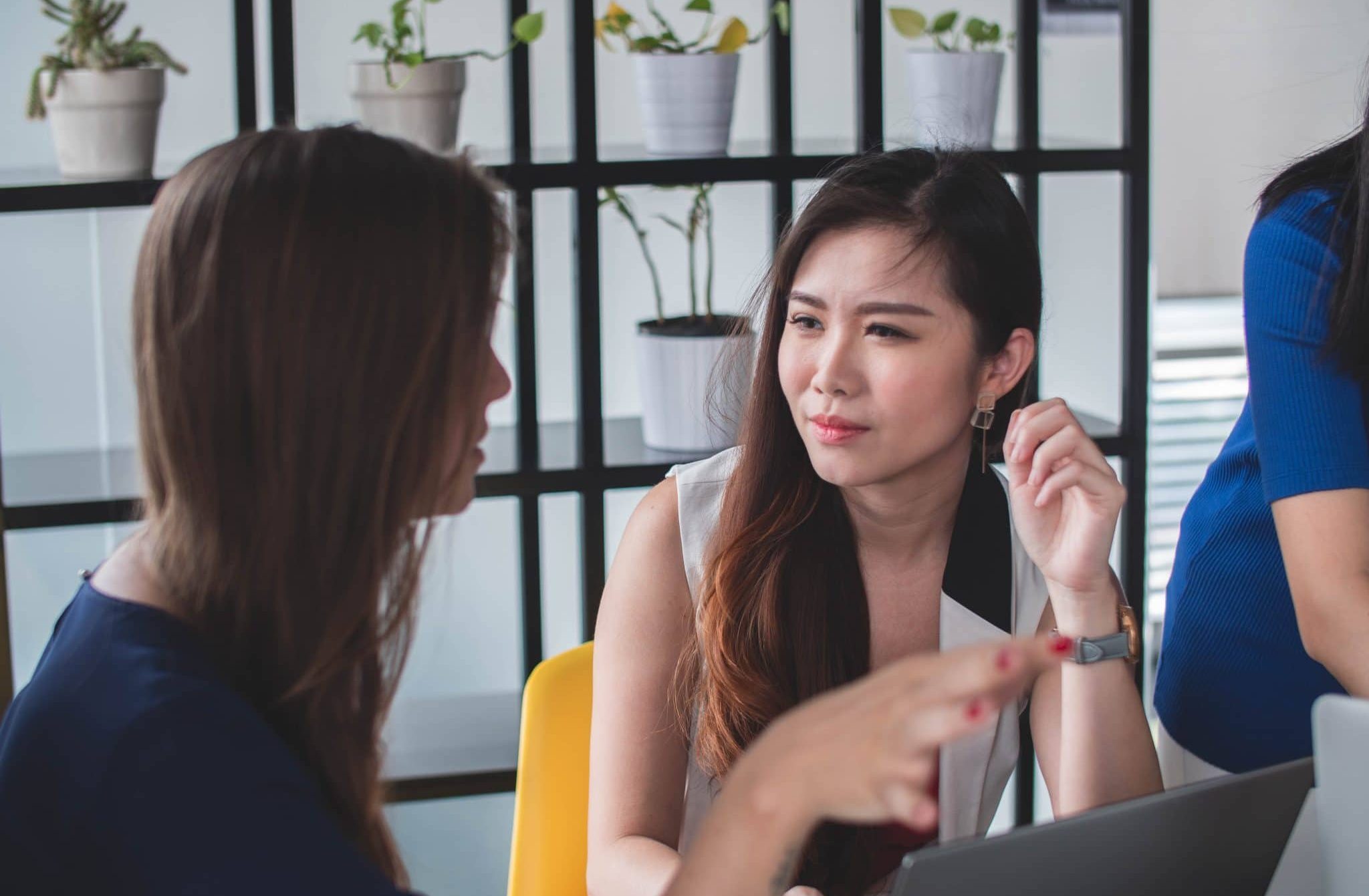 Photo of two women sitting on a desk, one is talking whilst the other is listening.