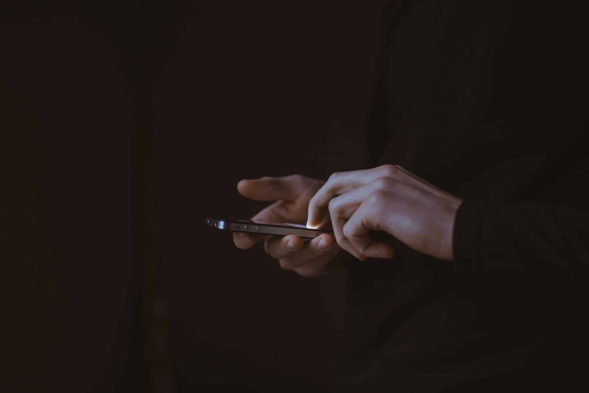 Photo of a woman's hands taken as she's on her smartphone in a room with a black background.
