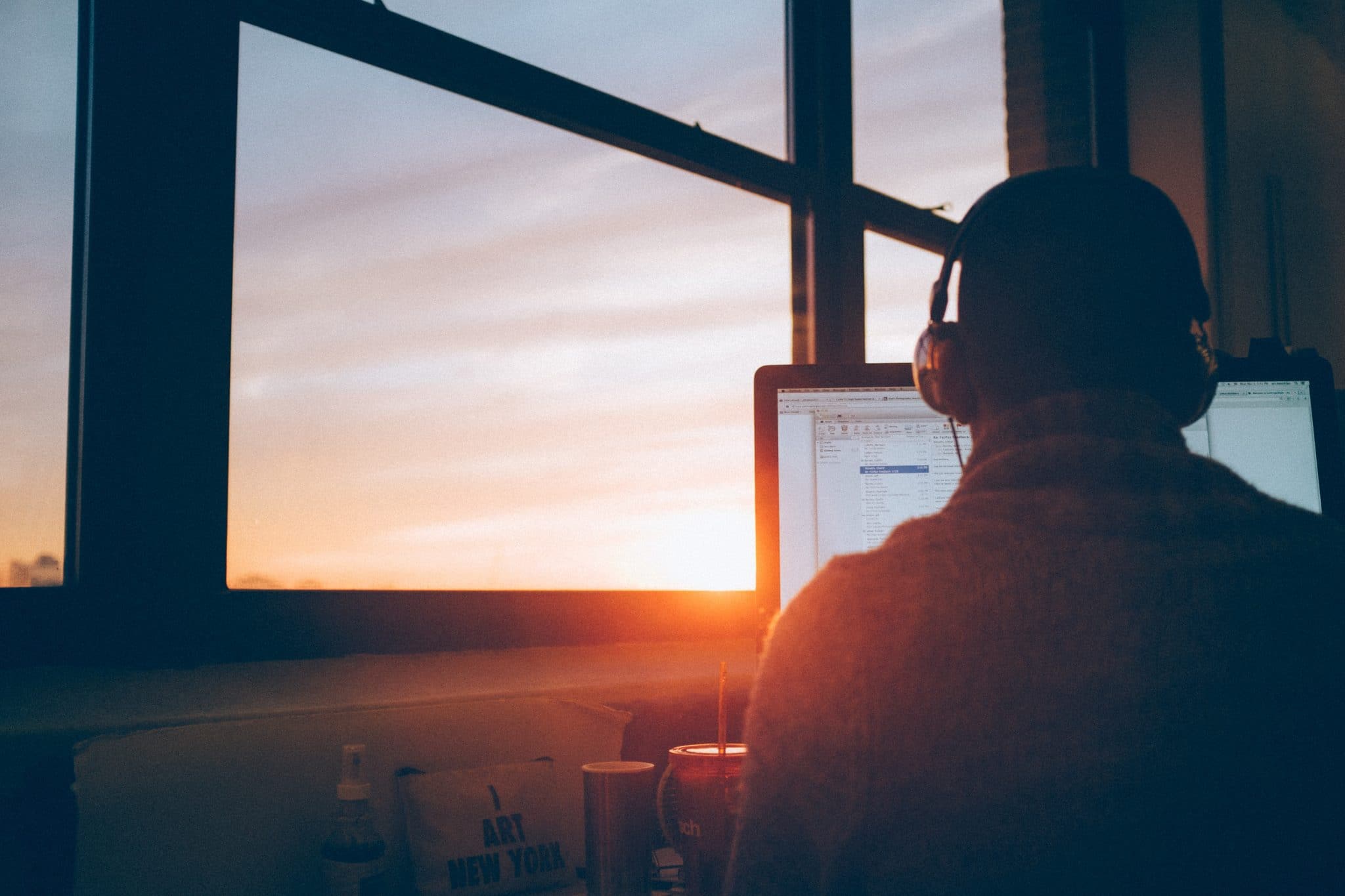 Man wearing headphones whilst sitting in the sunset facing a PC monitor.