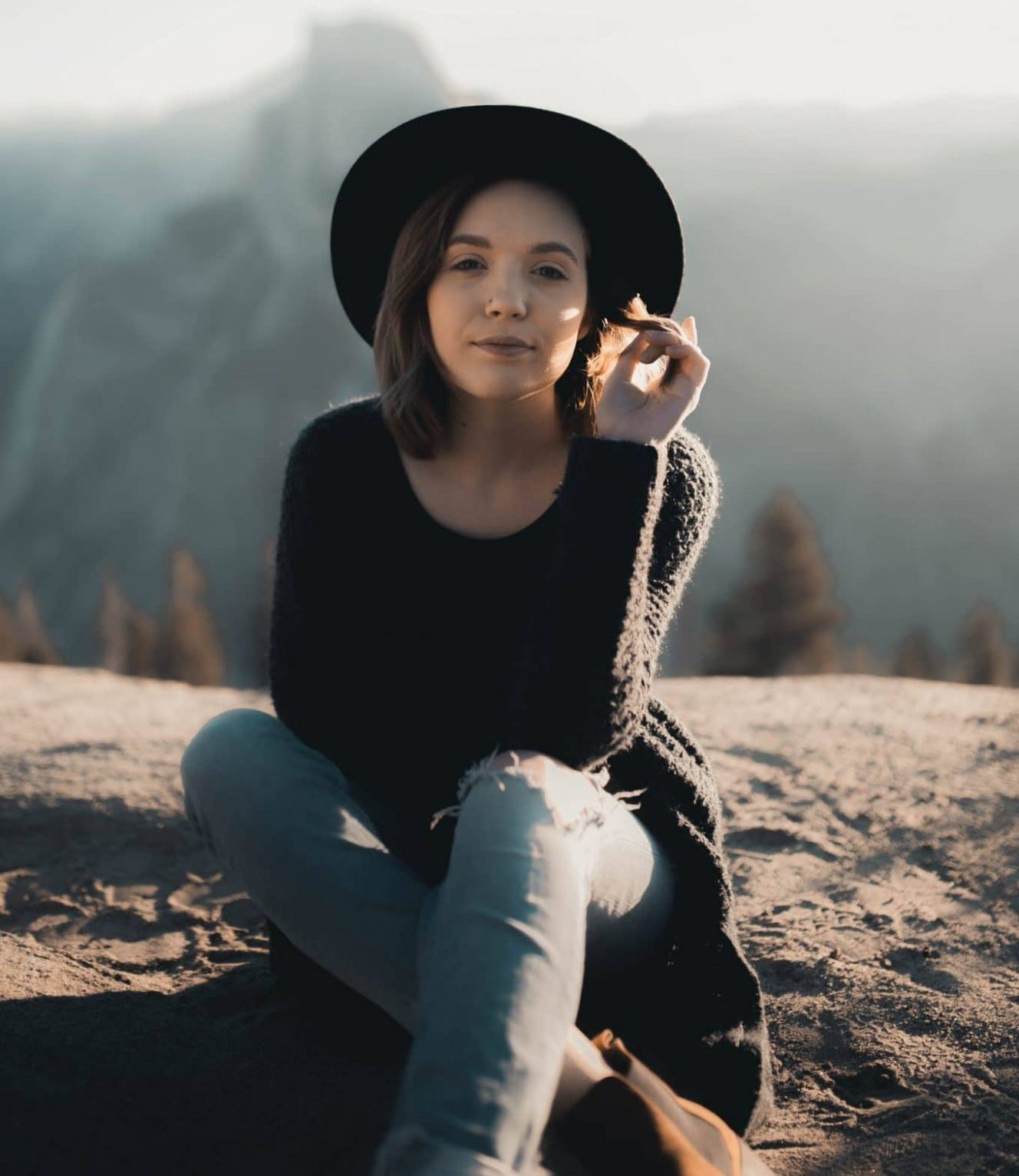 Woman sitting on mountain top wearing a stylish hat in a picturesque environment
