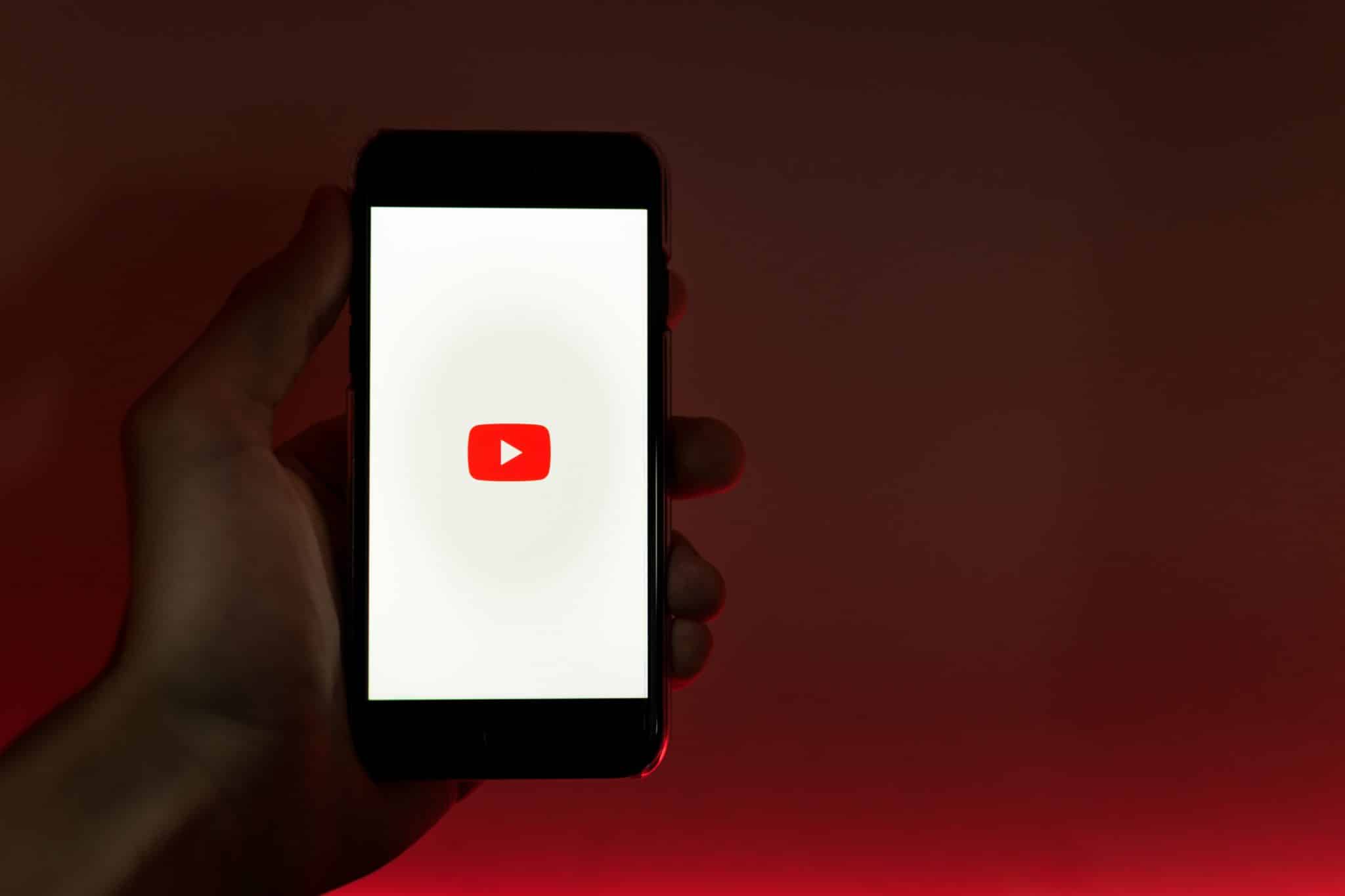 Photo of a person holding a smart phone showing the YouTube logo.