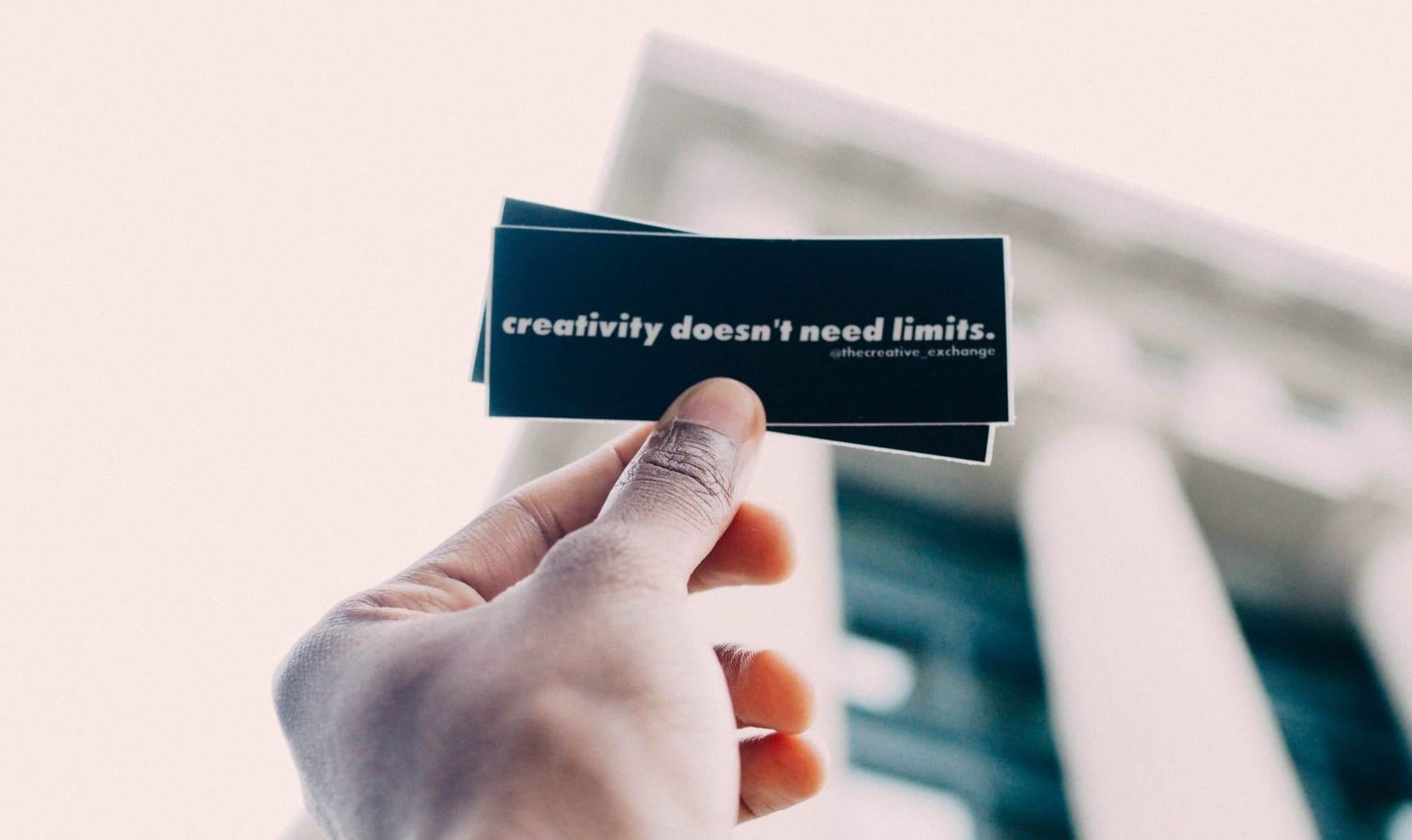 Photo of a man's hand holding a business card with a quote, "creativity doesn't need limits".
