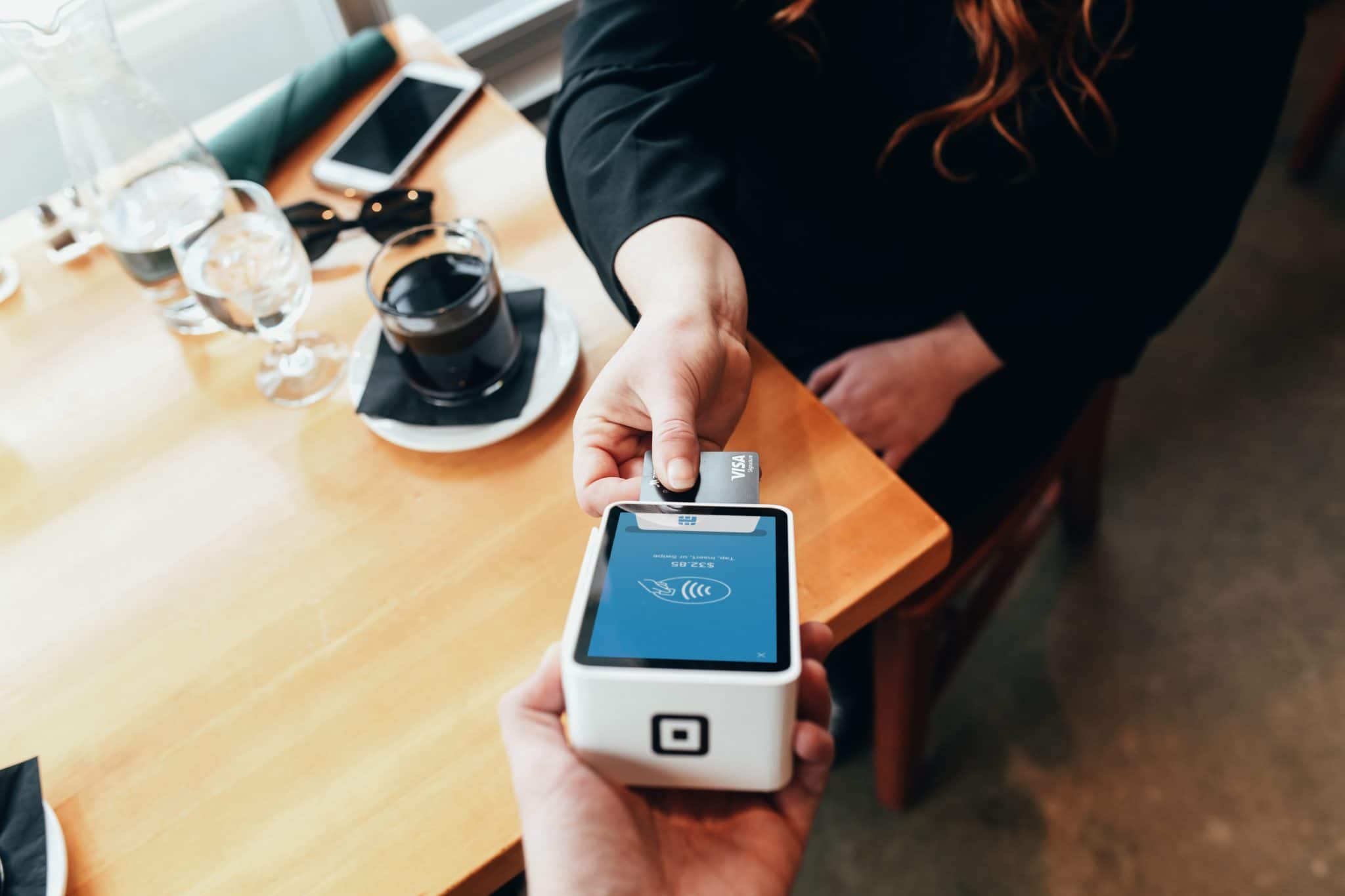 Photo of two people one making a sale using a credit card machine whilst the other makes a payment using a visa card