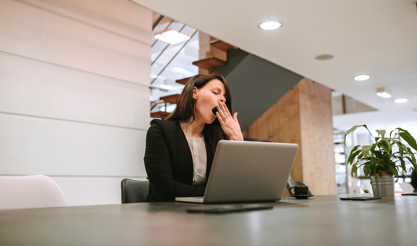 Photo of a business woman sitting and yawning in front of her laptop on her office desk.