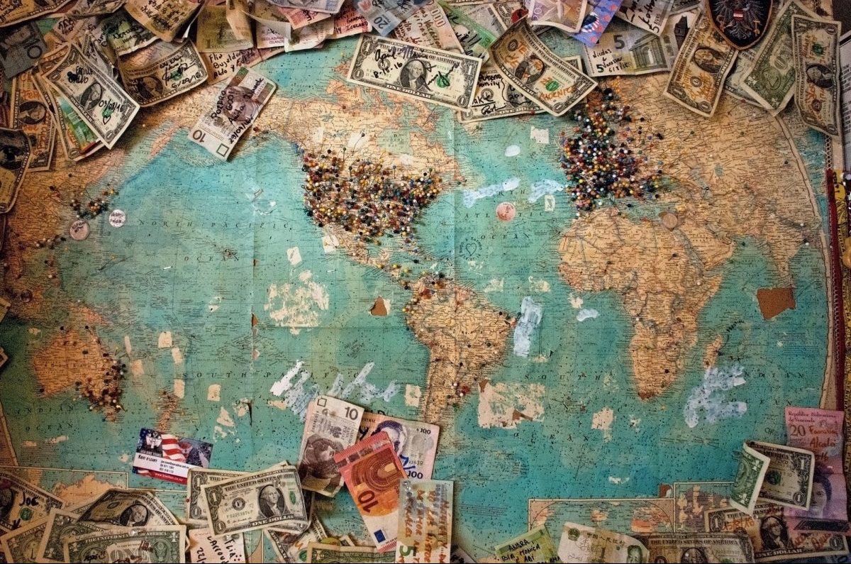 Map of world on flat desk with different international currencies also on top of the atlas to represent global business.