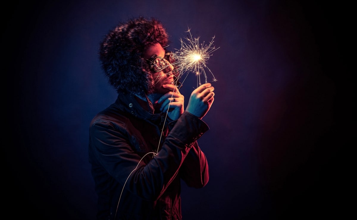 Photo of a man holding a fire-cracker in the dark, looking like he's stressed whilst trying to think of a bright idea.