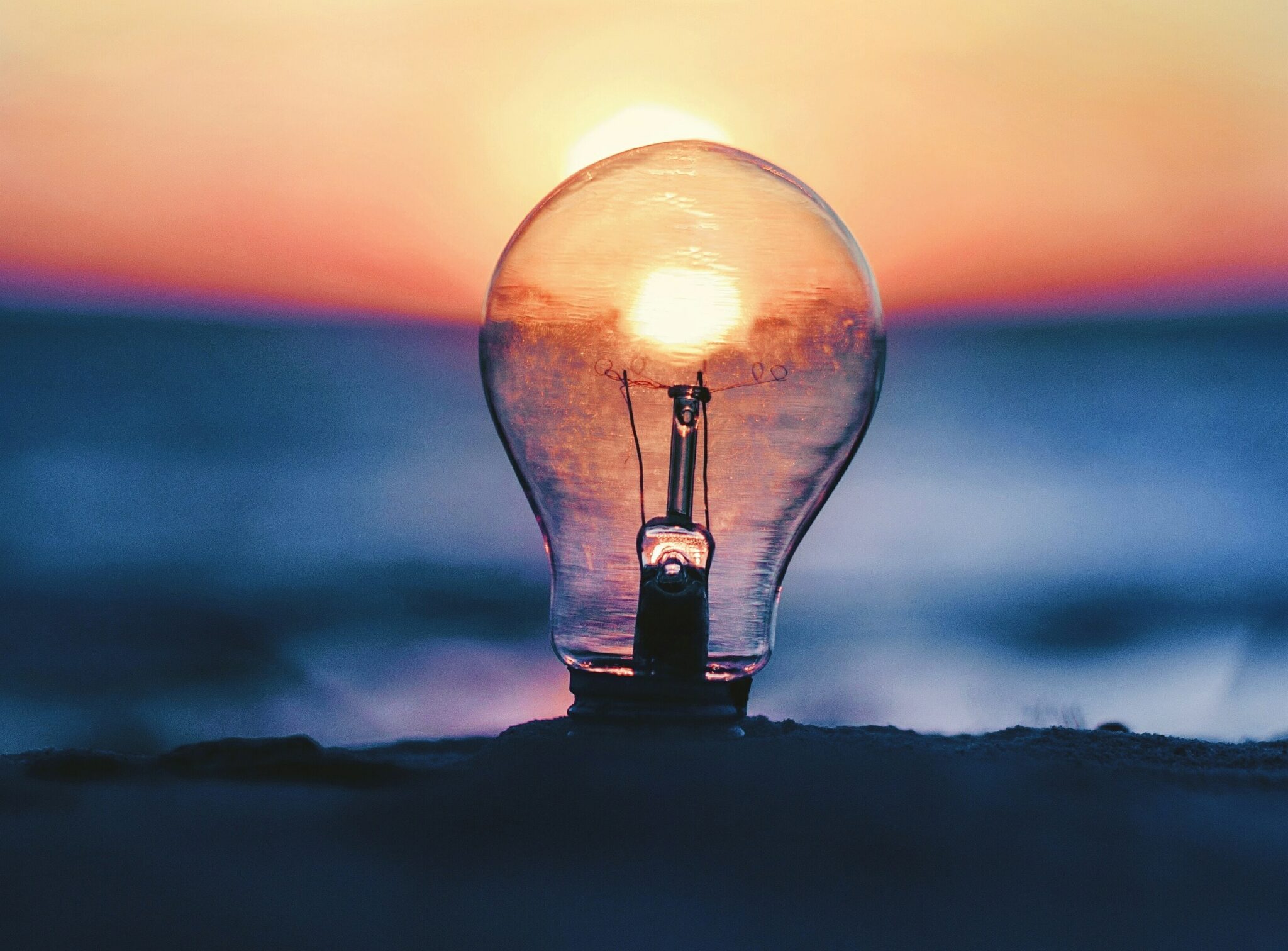 Lightbulb in the seaside, without electric power, showing the sunset in the middle of the bulb as the light.