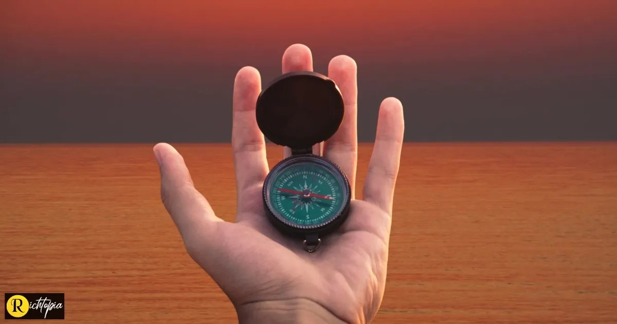 Photo of a man's hand holding a compass out to the sea during sunset