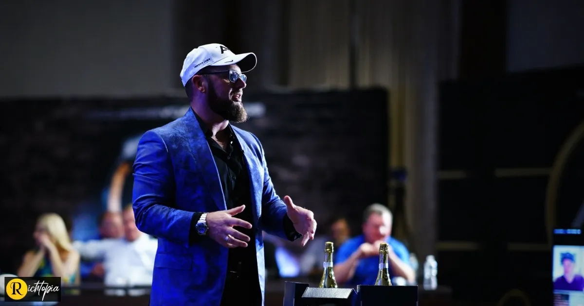 Photo of Mike Calhoun wearing a nike cap, blue blazer, and fashionable glasses while giving a keynote speech to an audience sittign on tables