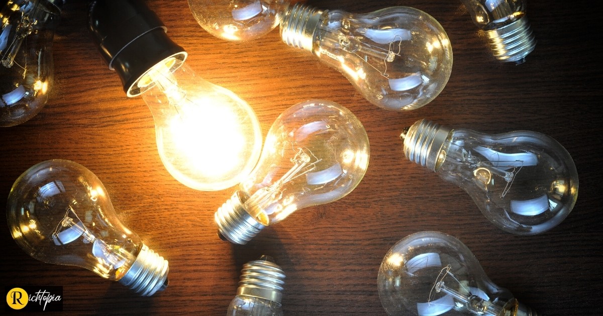 Photo of multiple light bulbs on a wooden table, with one of them illuminated.